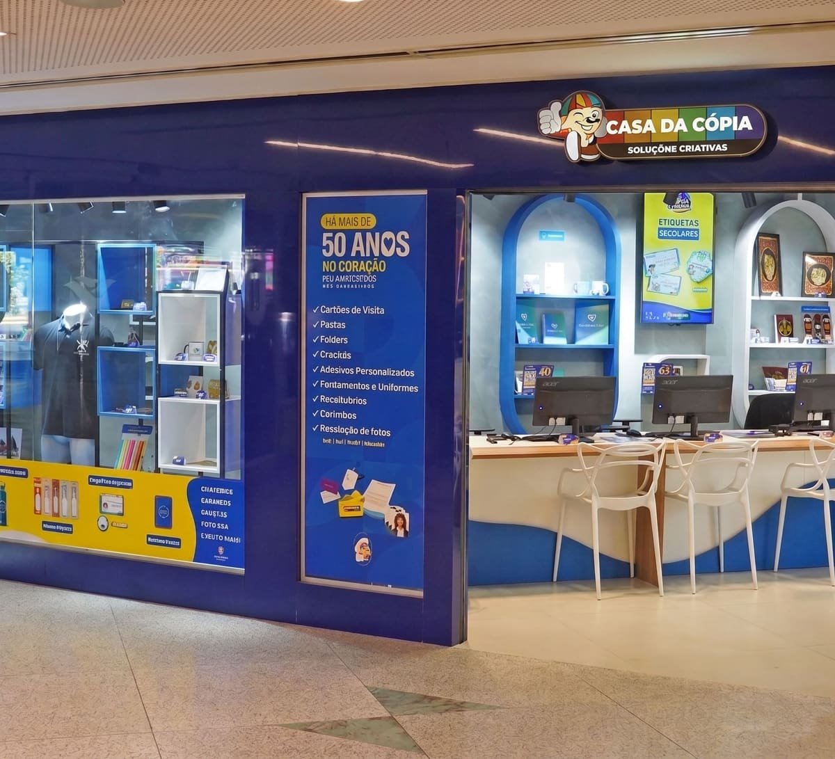 Balcão de atendimento de uma loja Casa da Cópia em shopping, com estações de computador e vitrine de brindes